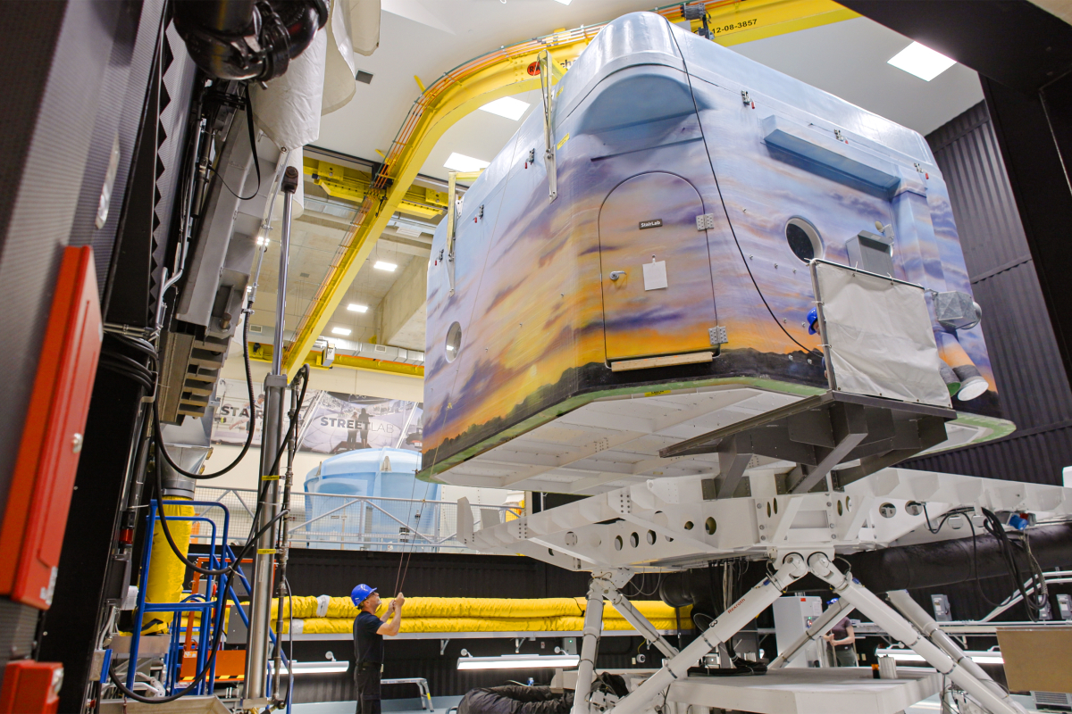 A worker holds guidelines as StairLab is lowered onto the hexapod motion base with an overhead crane. 