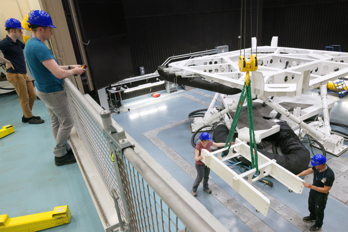 Workers guide a support structure to the motion base with a crane. 